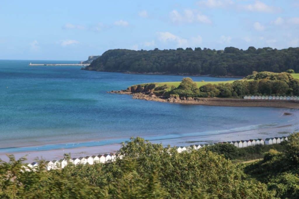 A serene, expansive sandy beach with footprints in the sand, set against a backdrop of rolling hills and distant mountains under a clear blue sky.