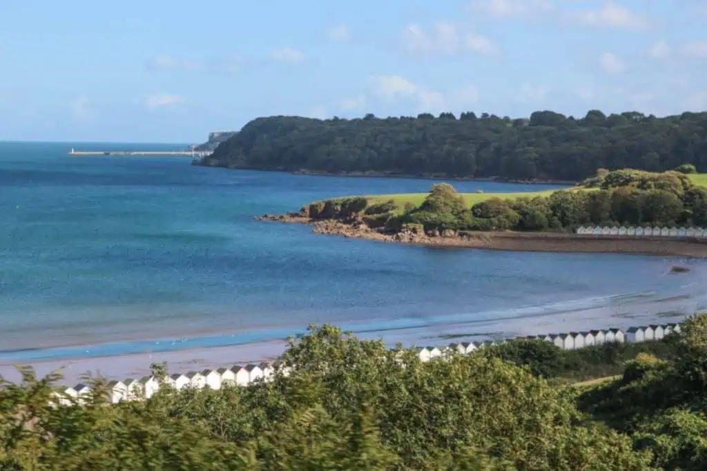 A serene, expansive sandy beach with footprints in the sand, set against a backdrop of rolling hills and distant mountains under a clear blue sky.