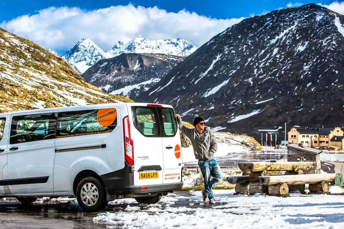 Traveller posing next to campervan in a snowy area - typical winter road trip in Europe