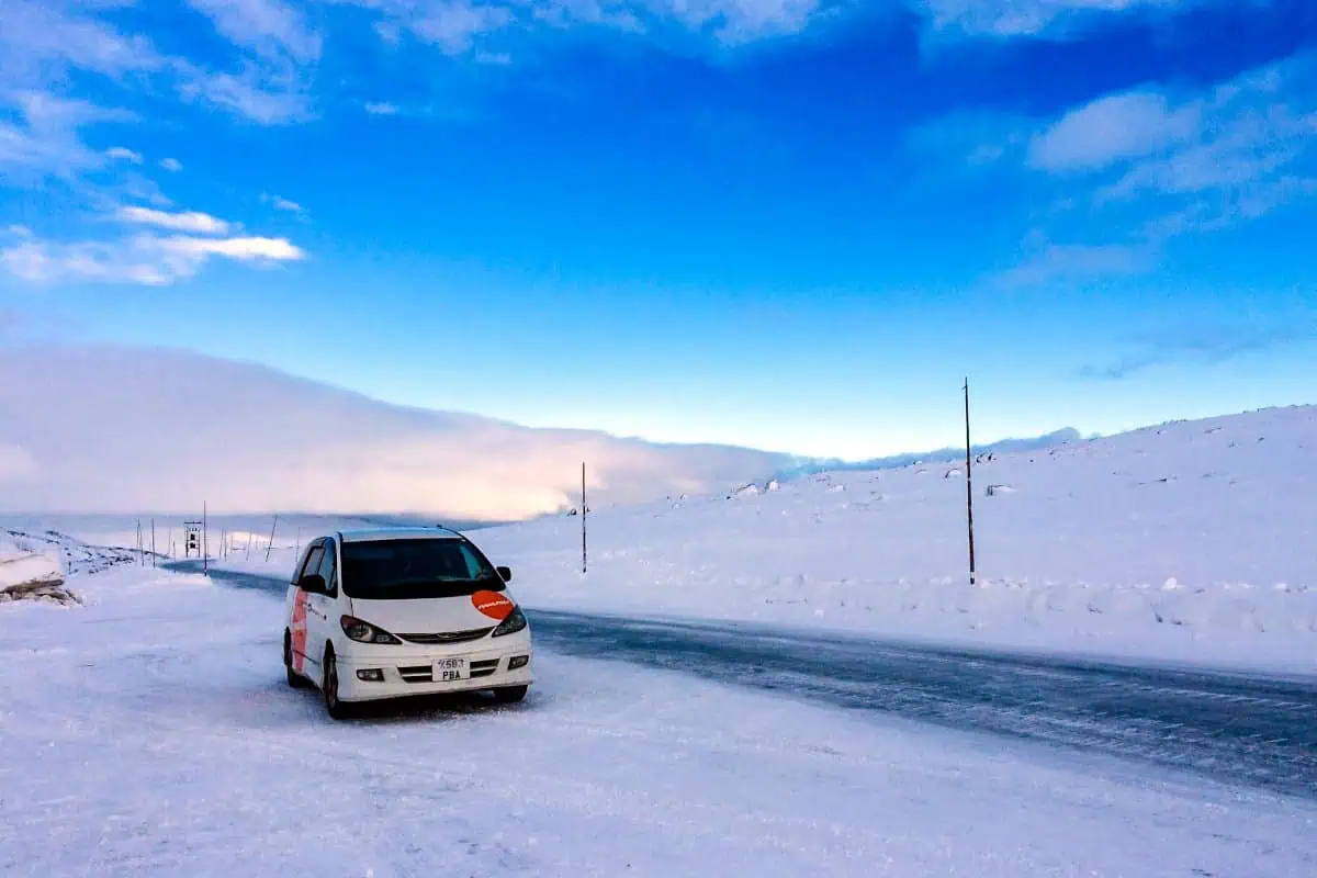 Compact campervan on a snowy road. Van on the left, snow everywhere, except on the road