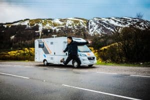 Motorhome parked in front of a hill and travellers jumping in front of it