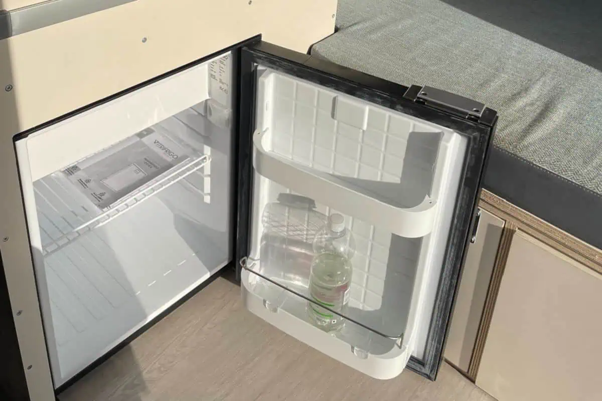 Open refrigerator inside the VW Cosmo Campervan, with a bottle of water on the shelf.